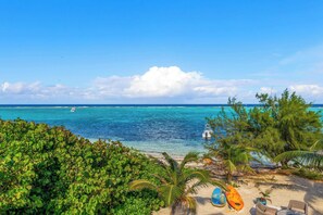 A beach view with clear turquoise waters, a boat, and a lounge area with chairs and a table. - The Blue Iguana Oceanfront Studio Cottage in East End (East End)