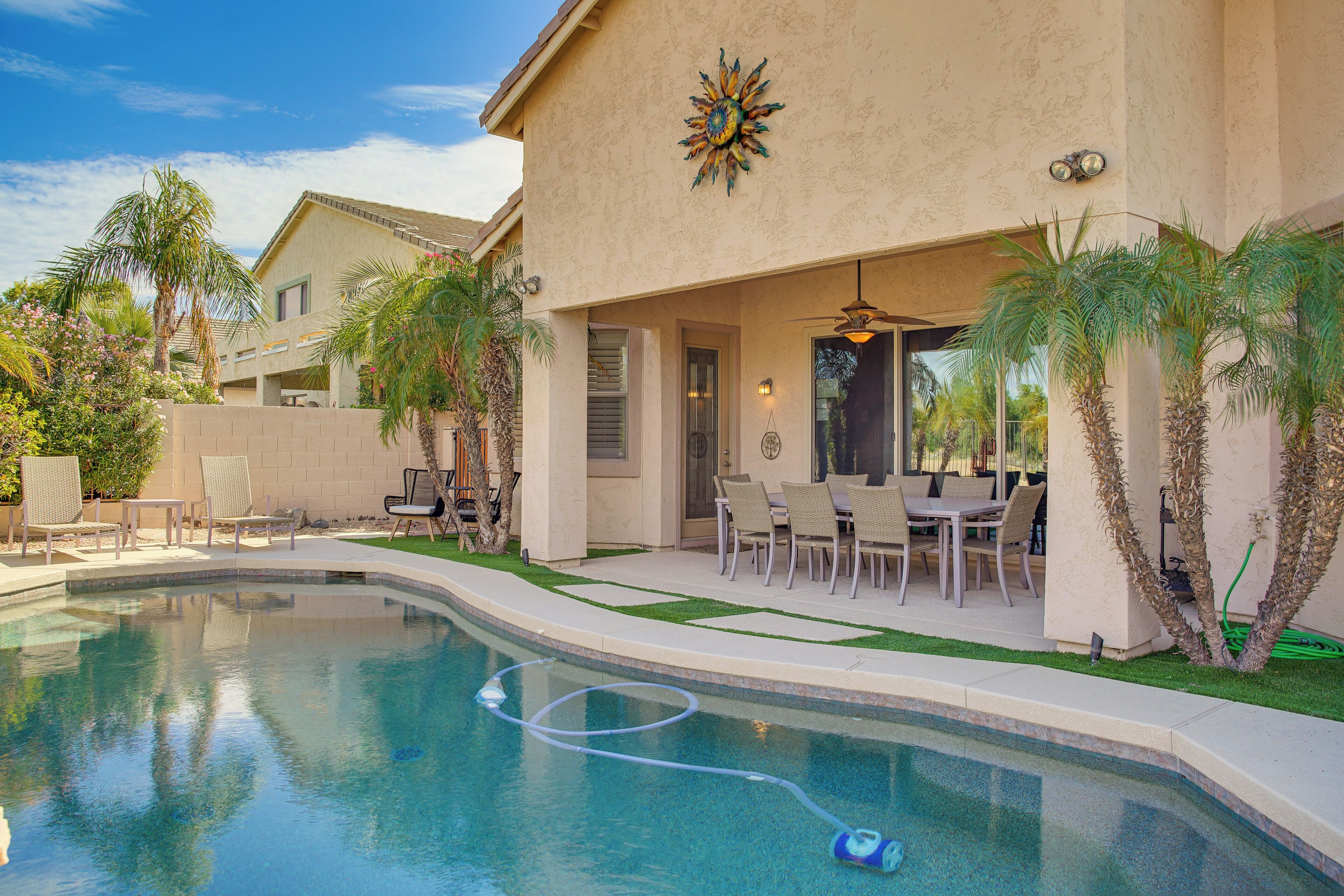 A swimming pool with a hose, outdoor furniture, and palm trees.