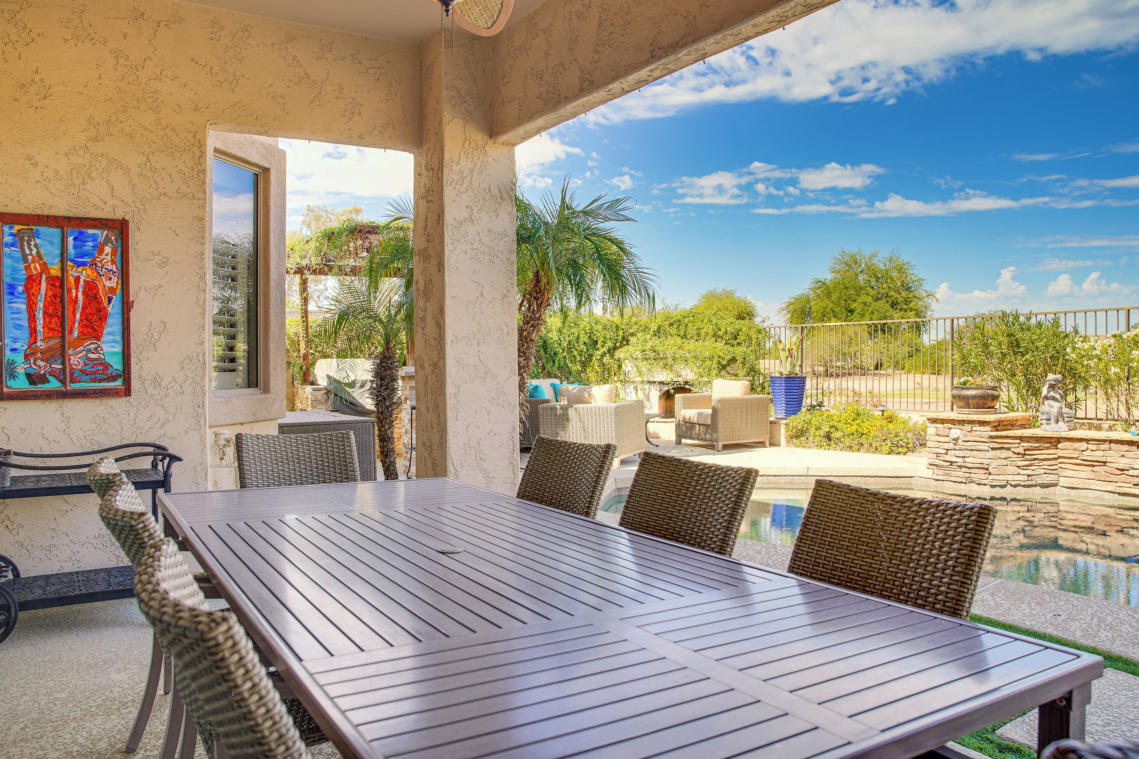 Eine überdachte Terrasse mit Esstisch und Korbstühlen, mit Blick auf einen Swimmingpool und üppige Vegetation.