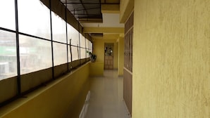 Un couloir avec de grandes fenêtres d’un côté, un sol carrelé et un mur jaune.