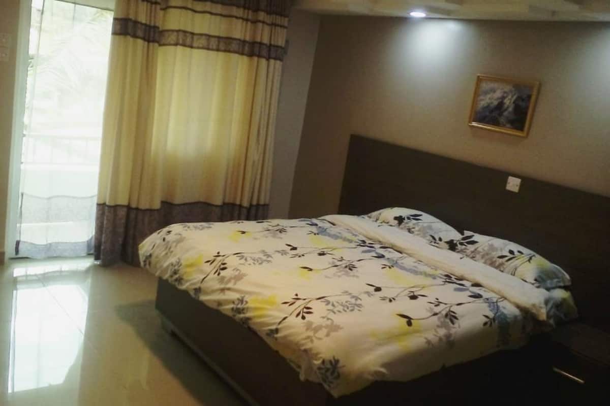 A bedroom with a bed, curtains, a painting on the wall, and a pair of slippers on the floor.