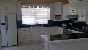 A kitchen with white cabinetry, a central island, and a window with blinds. - Belle View Rising (Gros Islet)