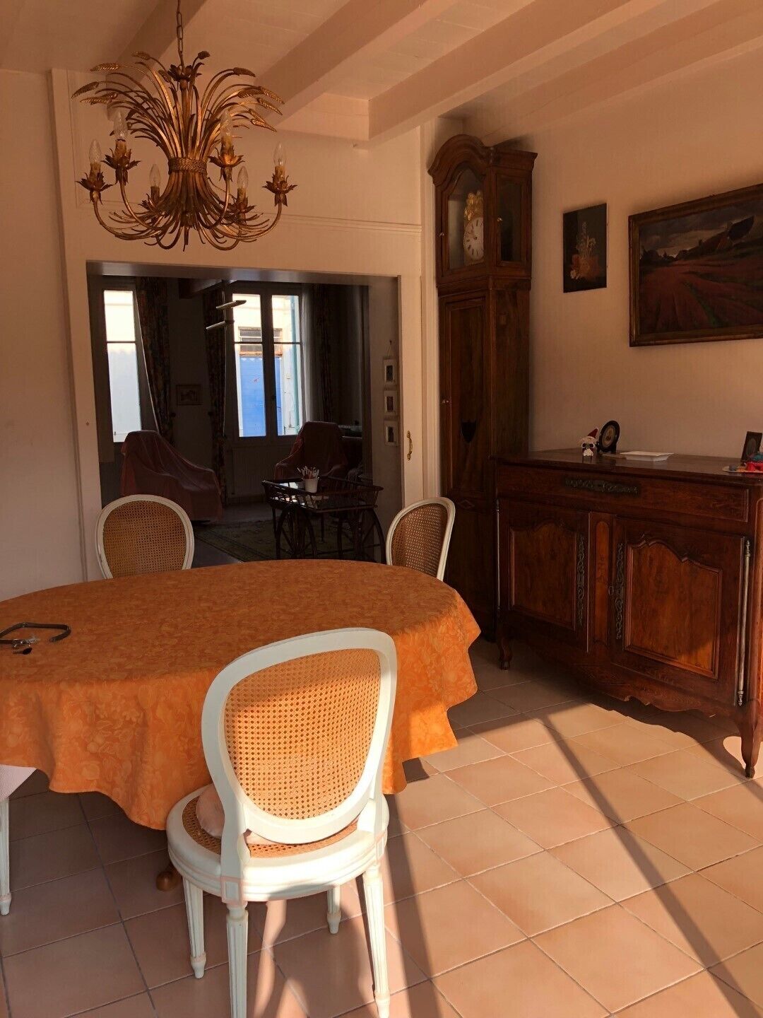 Un comedor con una mesa redonda, sillas blancas, una araña, un aparador de madera y un cuadro en la pared.