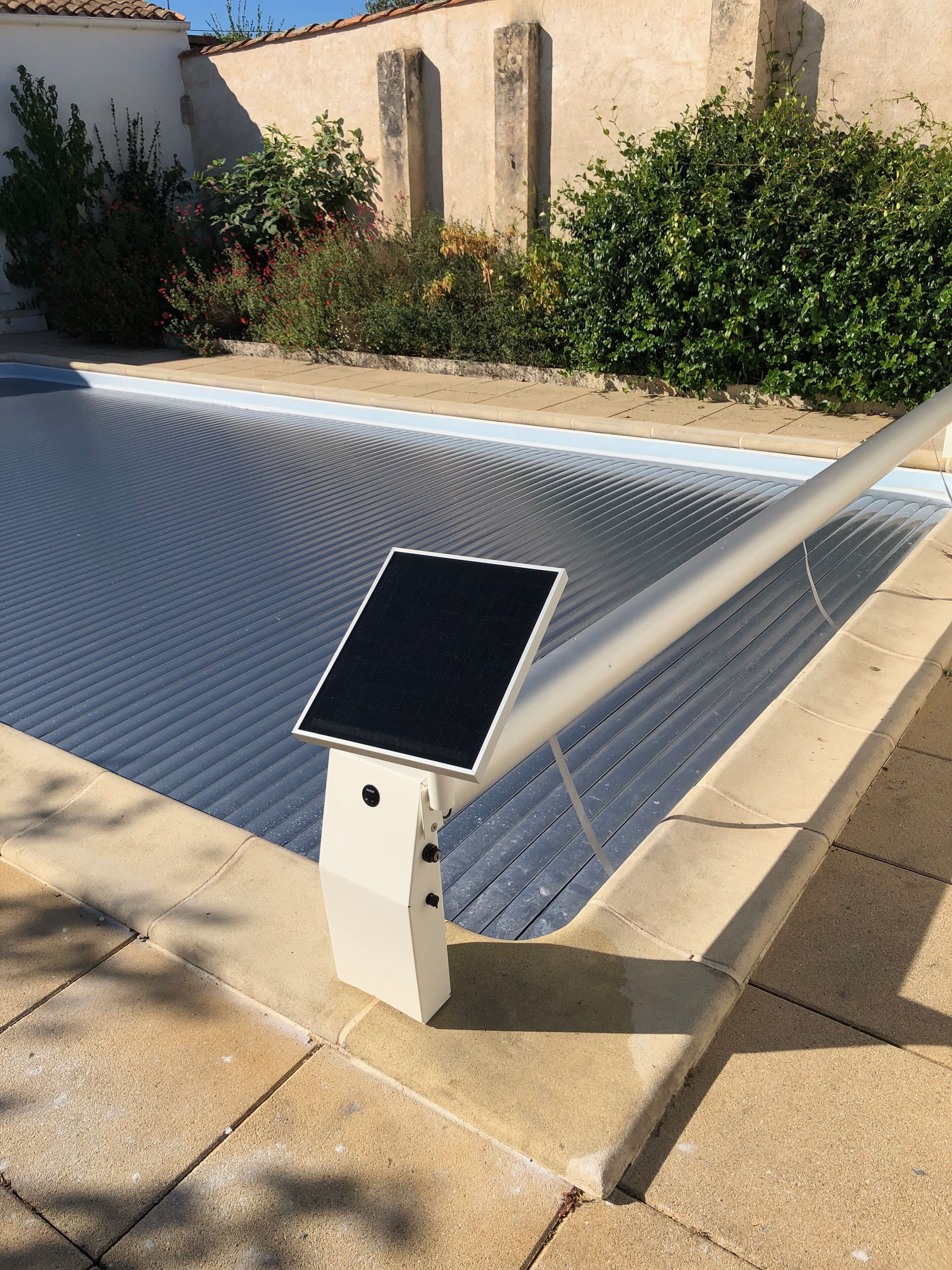 Une piscine chauffée à l’énergie solaire, dotée d’un panneau de commande, entourée d’une terrasse carrelée et de verdure.