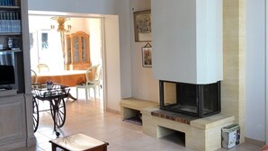 A living room with a fireplace, a bookshelf, a dining area, and a patterned rug.