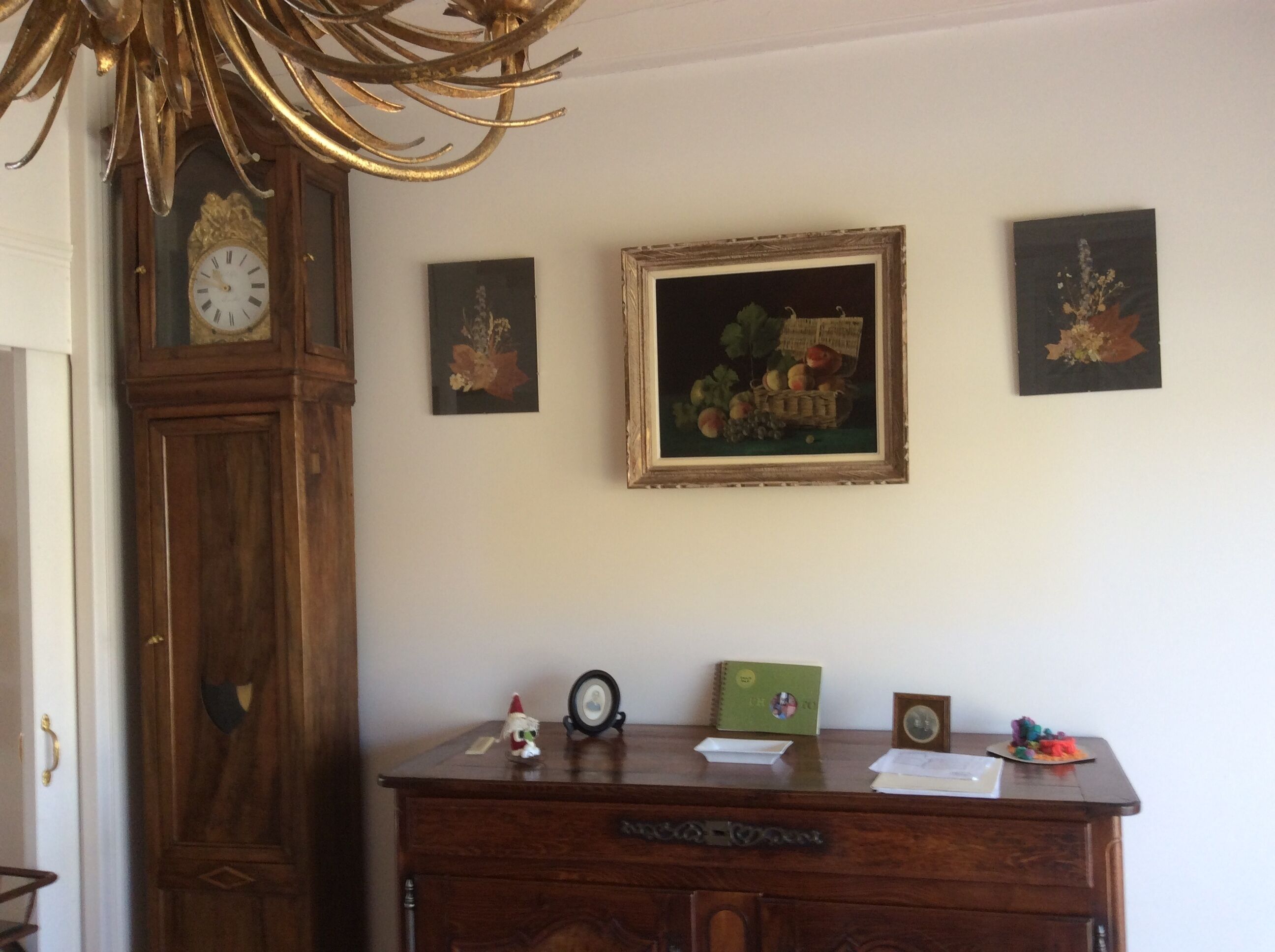 Een kamer met een houten dressoir, een grote klok en drie ingelijste kunstwerken aan de muur.