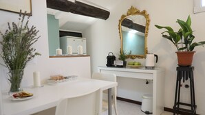 A white dining table with chairs, a mirror, a potted plant, and a white cabinet with candles.