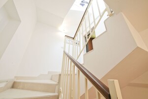 A modern staircase with a wooden handrail and glass railings, leading to an upper floor.