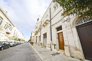 A cobblestone street lined with historic buildings, parked cars, and a closed shop with a dark shutter.