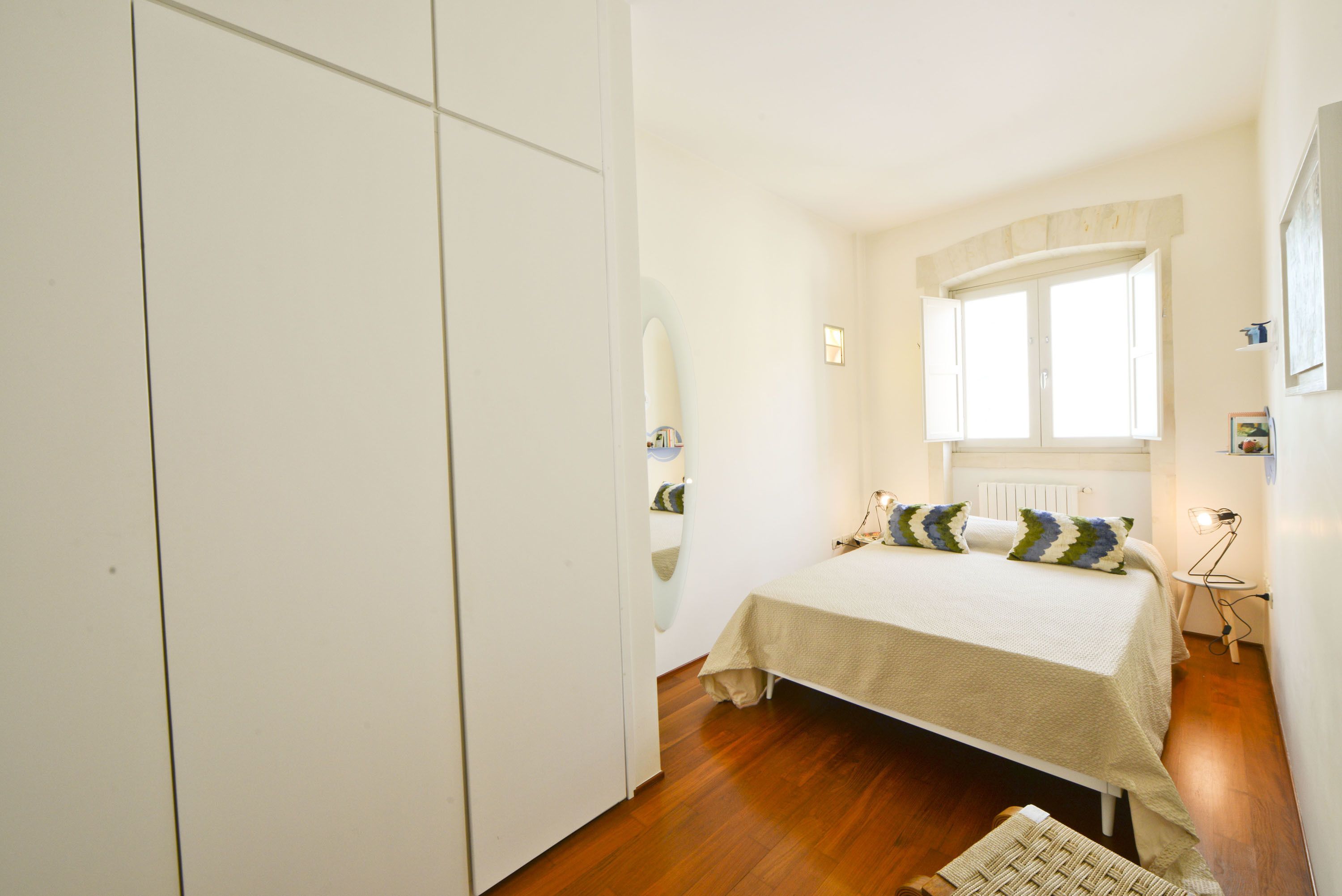 A bedroom with a bed, a wardrobe, a window, and a bedside lamp.