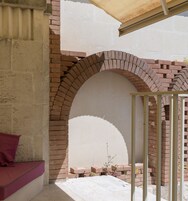 A brick archway leading to a covered outdoor area with a bench and a plant.