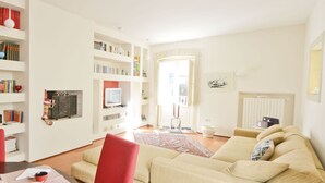A living room with a beige sofa, a red chair, a coffee table, and a bookshelf filled with books. - Appartamento Ambra con Balcone by Wonderful Italy (Ostuni)