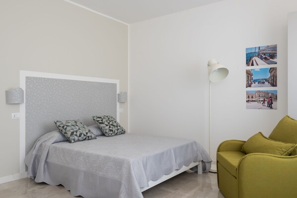 A bedroom with a bed, a nightstand, a lamp, and a wall with photos. - Wonderful Italy Suites (Syracuse)