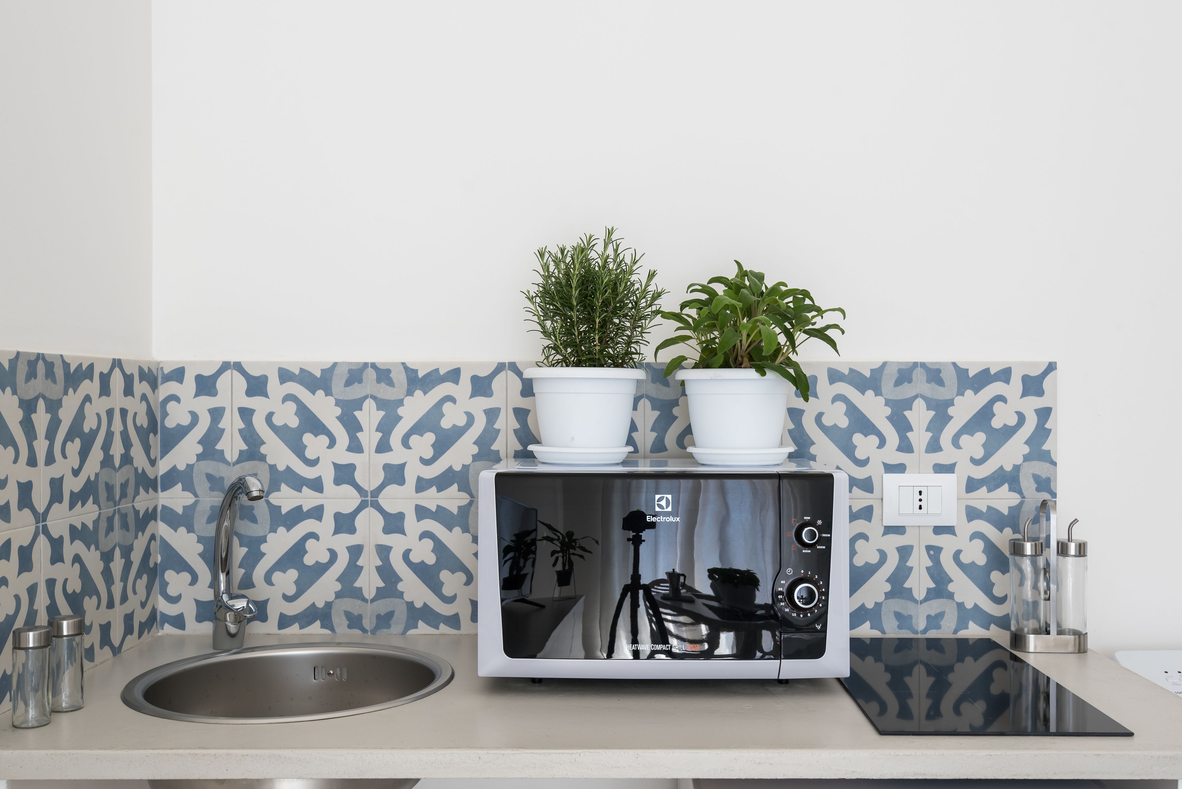 A kitchen with a modern stove, a sink, and two potted plants on the countertop.