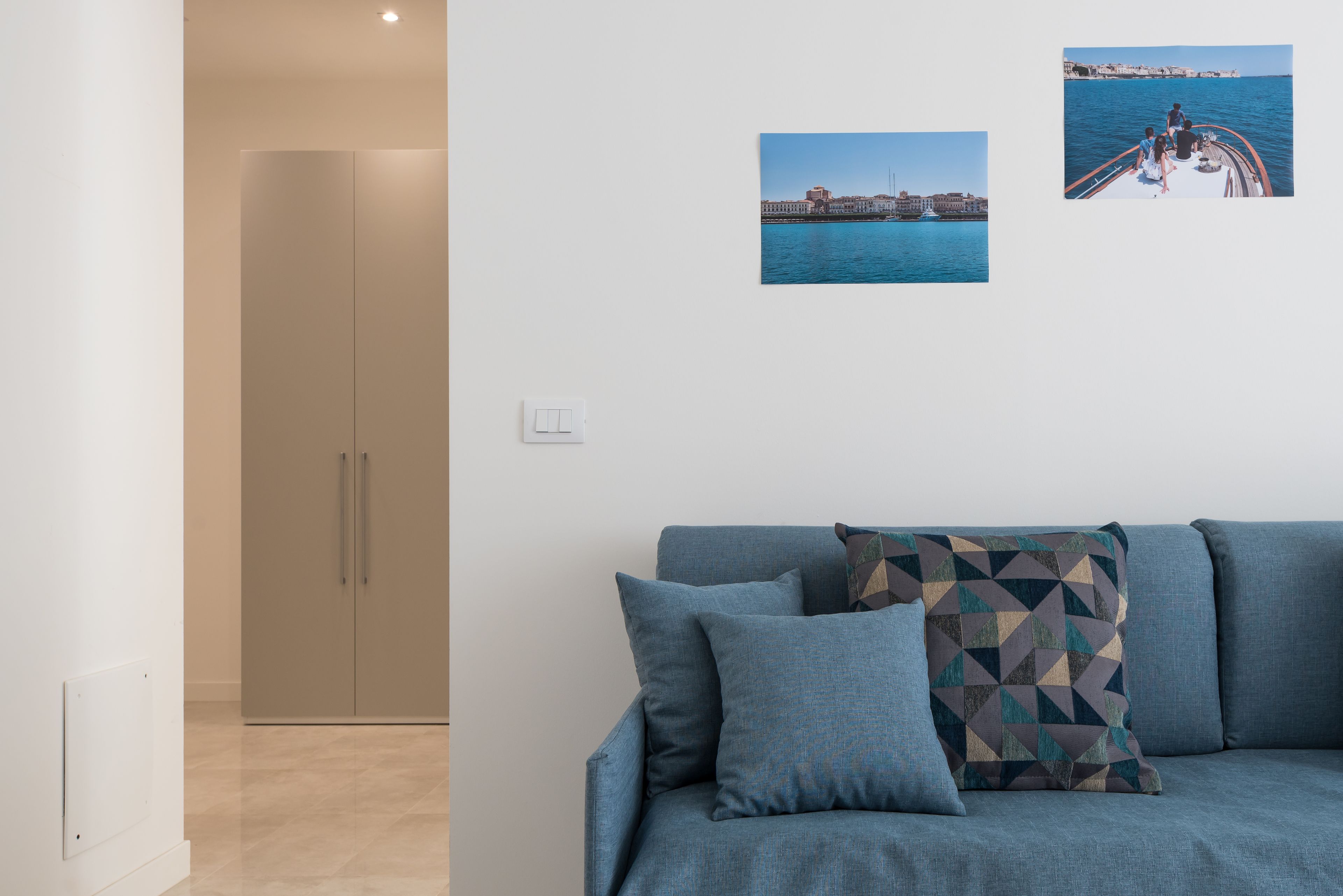 Ein modernes Wohnzimmer mit einer Couch, einem Kissen mit geometrischem Muster und zwei gerahmten Fotos an der Wand.