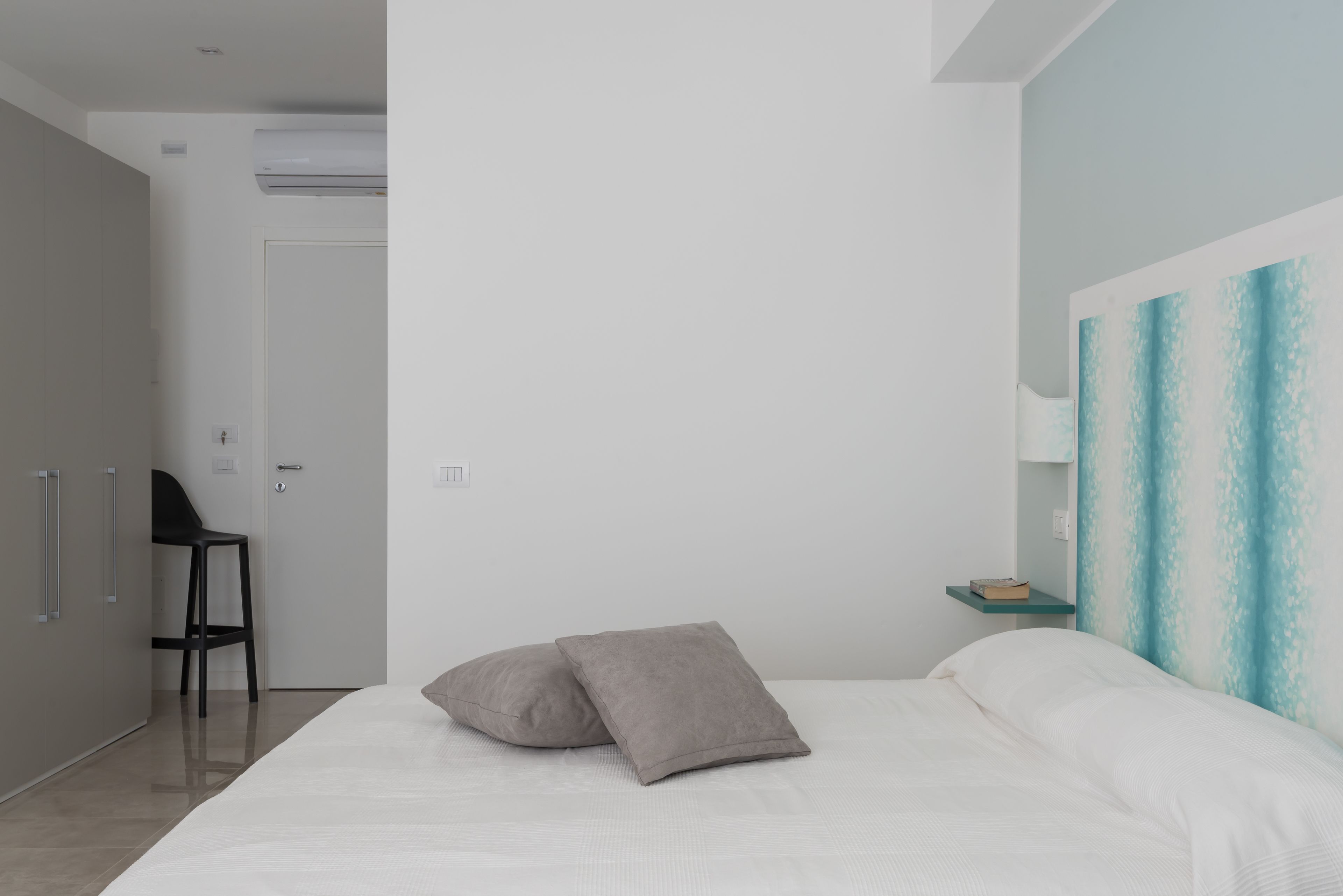 Une chambre à coucher avec un lit, deux oreillers, une chaise, une table de chevet et un tableau accroché au mur.