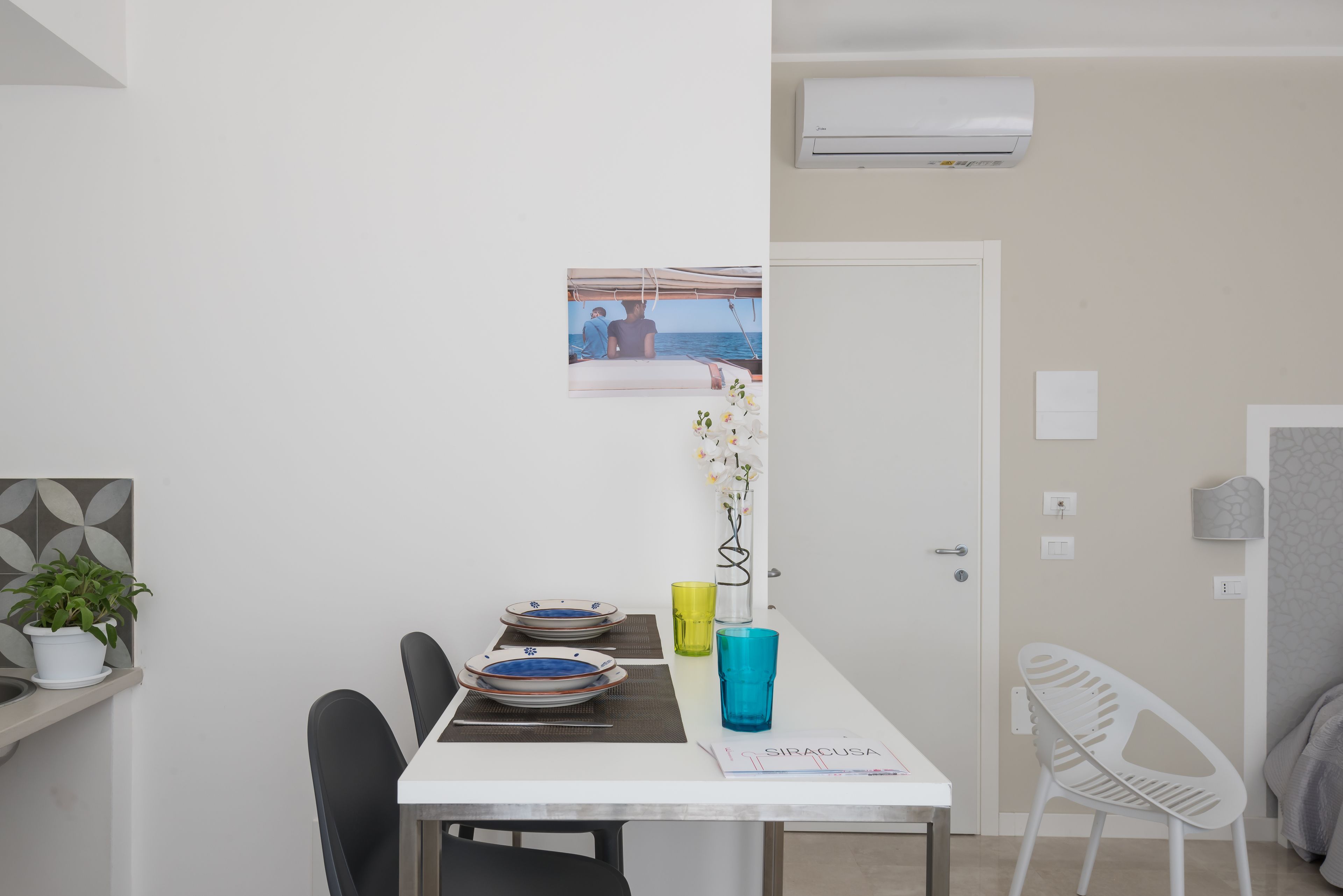 Ein Essbereich mit Tisch für zwei Personen, einem Blumentopf und einem gerahmten Bild von einer Strandansicht.
