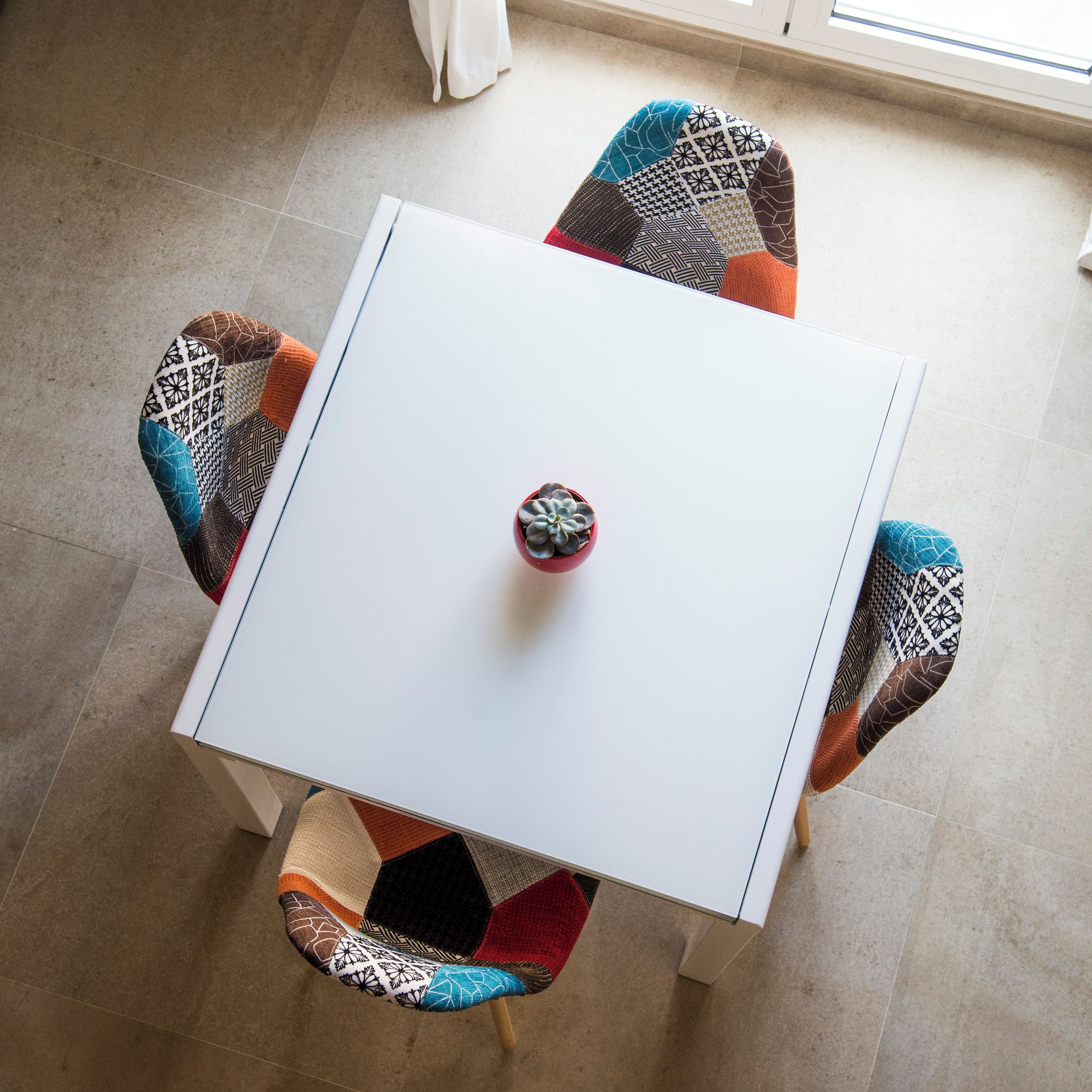 A white table with a small potted plant in the center, surrounded by four chairs with patterned upholstery.
