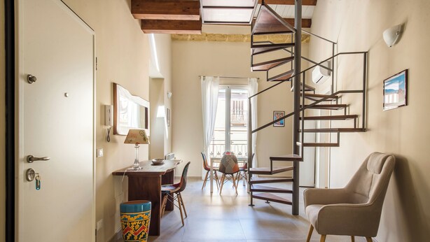 A hallway with a spiral staircase, a dining area with chairs and a table, and a beige armchair.
