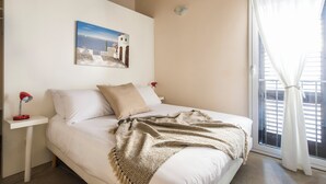 A bedroom with a bed, a nightstand, a lamp, a painting, and a window with curtains.