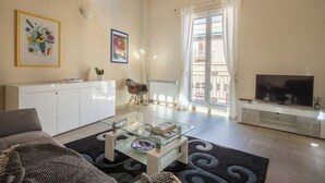 A living room with a glass coffee table, white sofa, and a TV on a stand.
