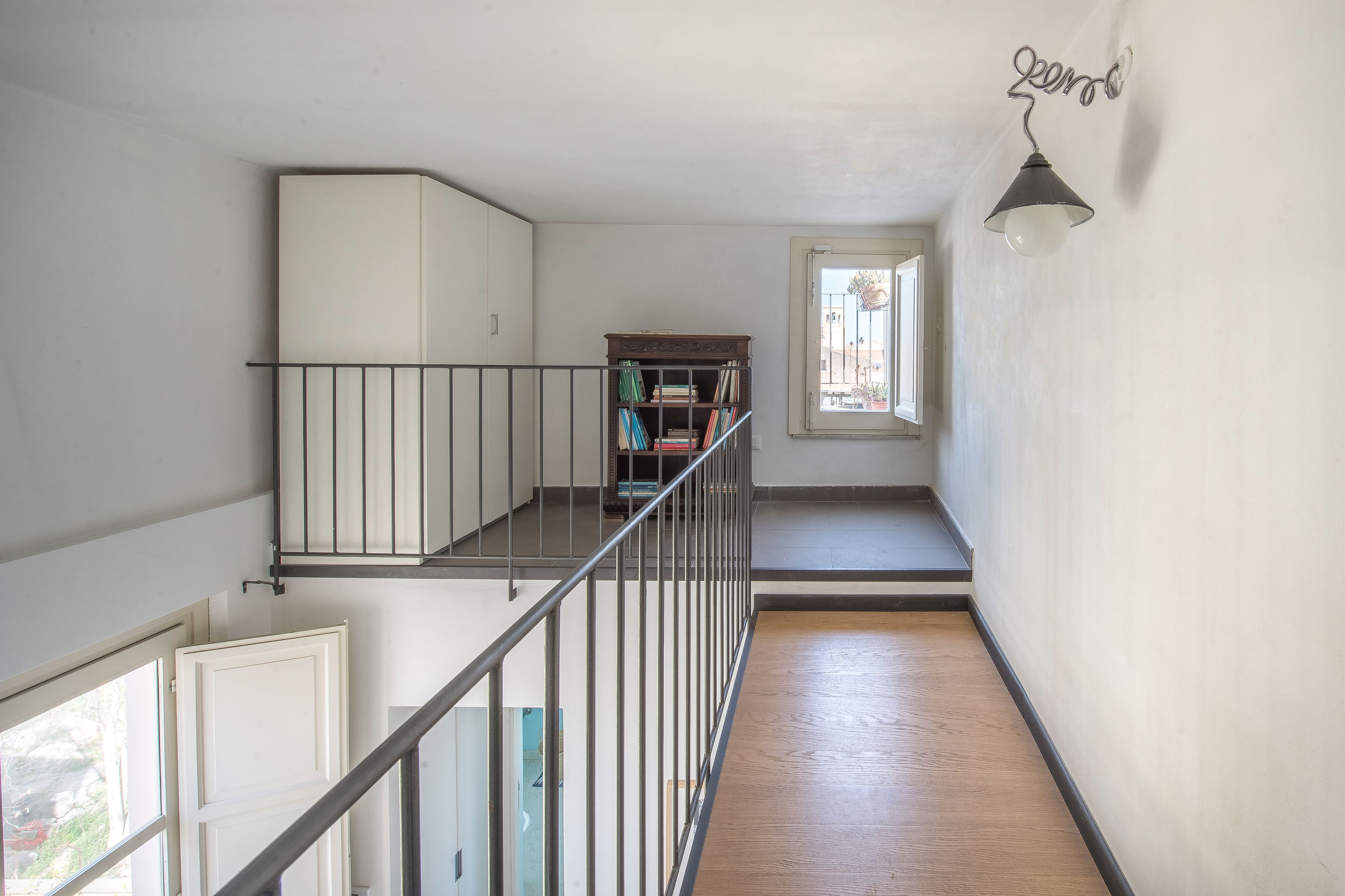 A spacious interior with a wooden floor, a metal railing, a white cabinet, and a window with a view.