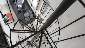 A spiral staircase with a metal railing, a gray sofa with cushions, and a window with a view of a mountain. - Palazzo Castrofilippo Apartment by Wonderful Italy (Palermo)