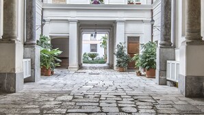 A courtyard with a stone floor, columns, and potted plants. - Palazzo Castrofilippo Apartment by Wonderful Italy (Palermo)