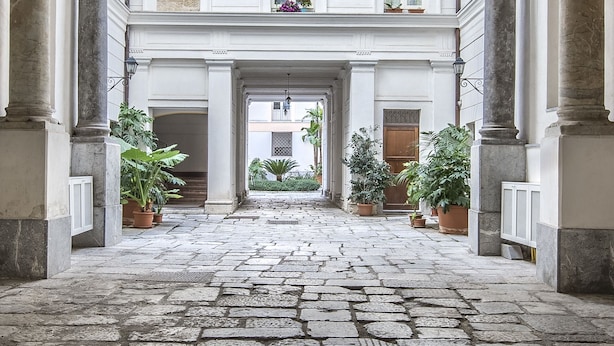 A courtyard with a stone floor, columns, and potted plants. - Palazzo Castrofilippo Apartment by Wonderful Italy (Palermo)