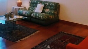 Een woonkamer met een groene bank, een rode fauteuil, een bijzettafeltje en drie abstracte schilderijen aan de muur.