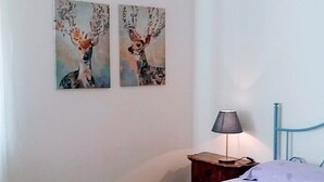 Een slaapkamer met een bed, een nachtkastje, een lamp en twee aan de muur hangende schilderijen.