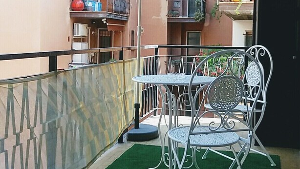 Een balkon met een tafel, stoelen, een plant in pot en een decoratieve parasol.