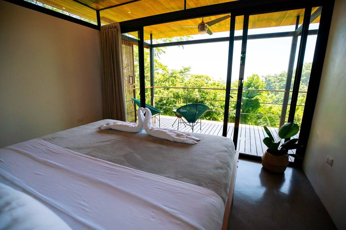 Une chambre d’hôtel avec un grand lit, un balcon donnant sur un espace verdoyant et un ventilateur de plafond.