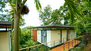 A modern house with a wooden deck and glass windows, surrounded by lush greenery. - The Green House - Santa Teresa (Cóbano)