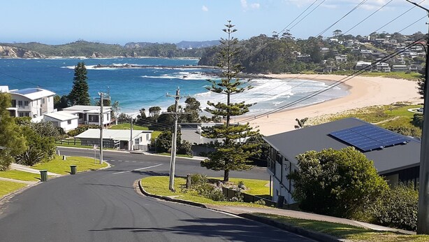 Une rue résidentielle bordée de maisons, avec une route et une plage en arrière-plan.