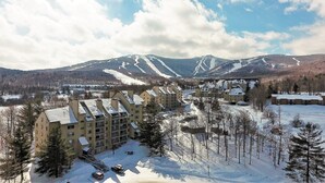A snow-covered mountain resort with multiple buildings, including a large hotel with a ski lift visible in the background. - The One Everyone Wants in Building 3 at Mountain Green: 1BR, Newly Renovated! (Killington)