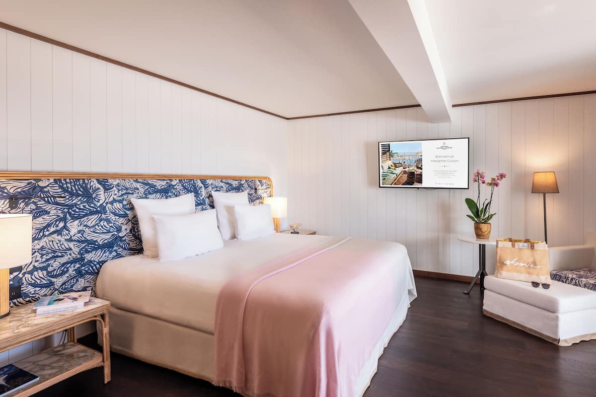 Ein Hotelzimmer mit einem großen Bett, einem an der Wand befestigten Fernseher, einem kleinen Tisch mit Pflanze und einem Sofa.