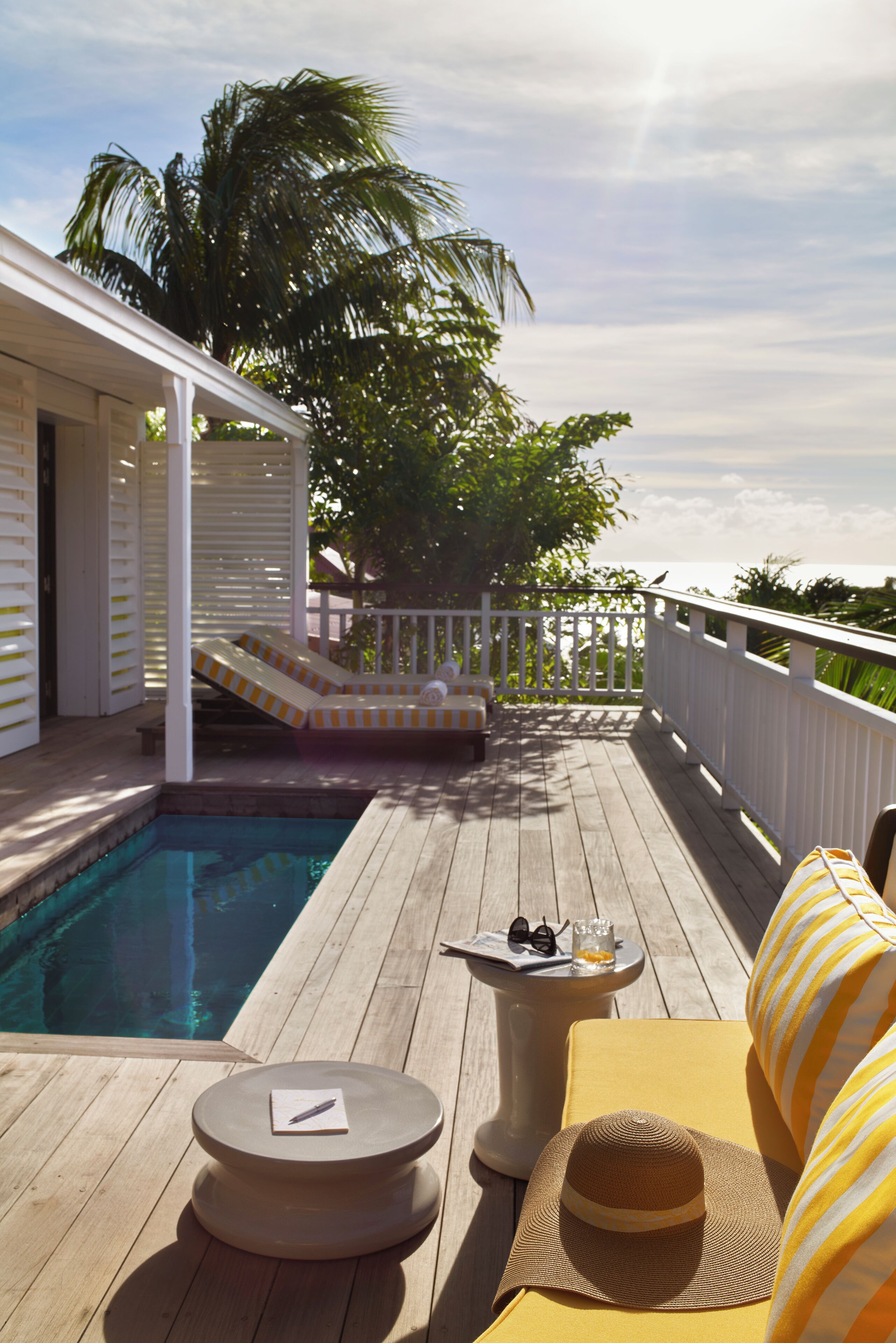 Eine Holzterrasse mit Pool, Liegestuhl, Sonnenliege und einem kleinen Tisch mit Hut und Sonnenbrille.
