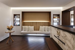 A spa reception area with a marble counter, a wooden bench with cushions, and a small table with a vase of flowers.