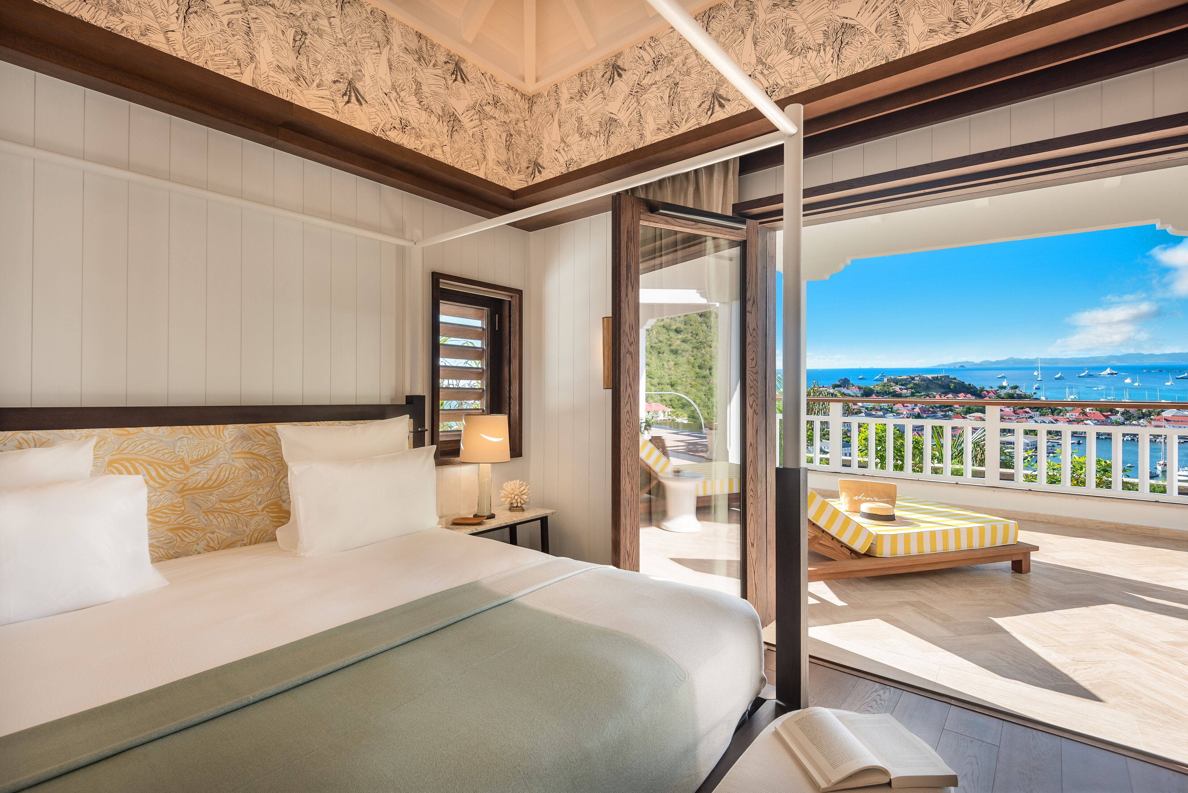 A hotel room with a large bed, a balcony with a view of the sea, and a dining area with outdoor furniture.