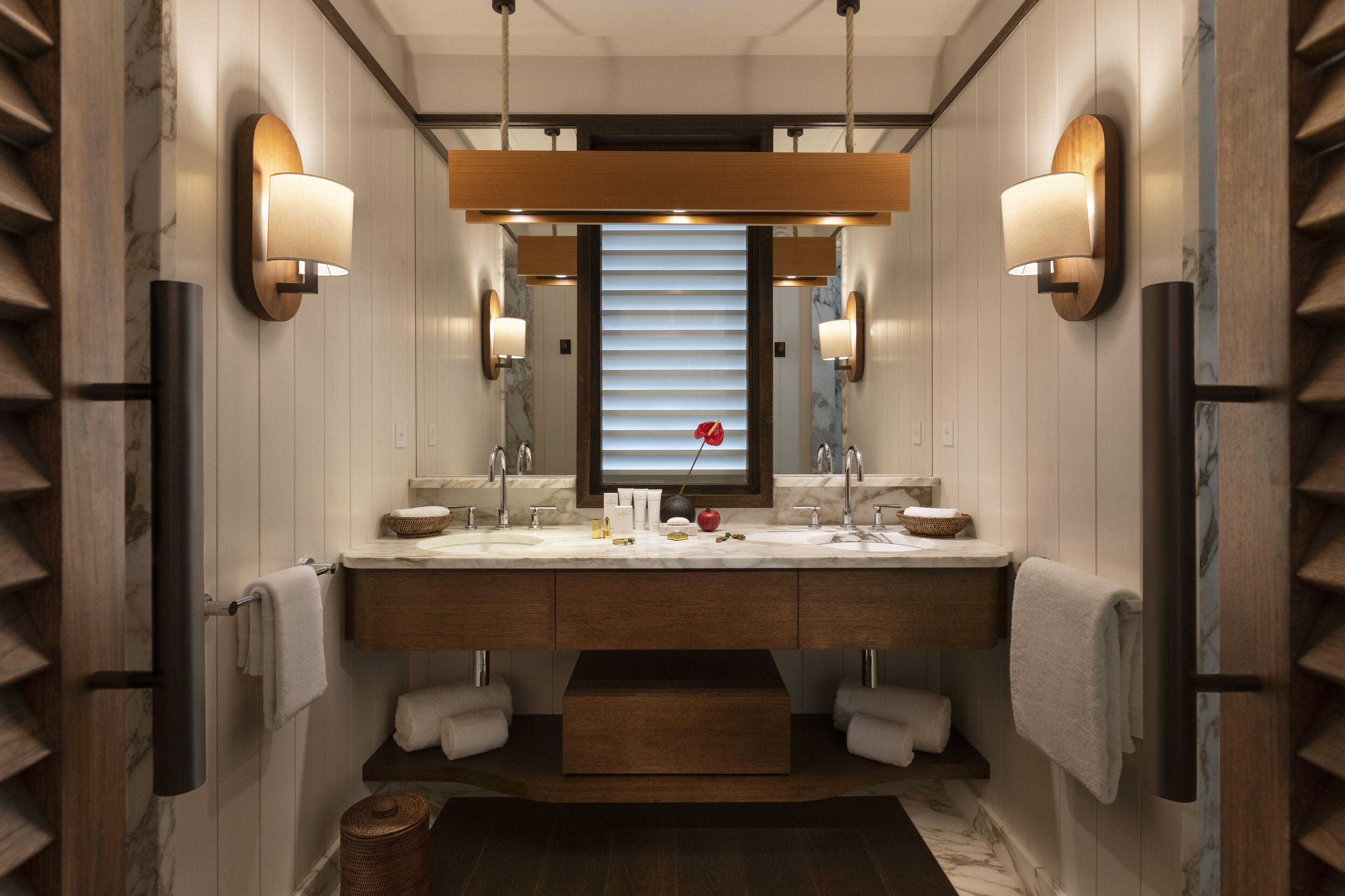 A modern bathroom with a double sink vanity, marble countertops, and wall-mounted lighting.