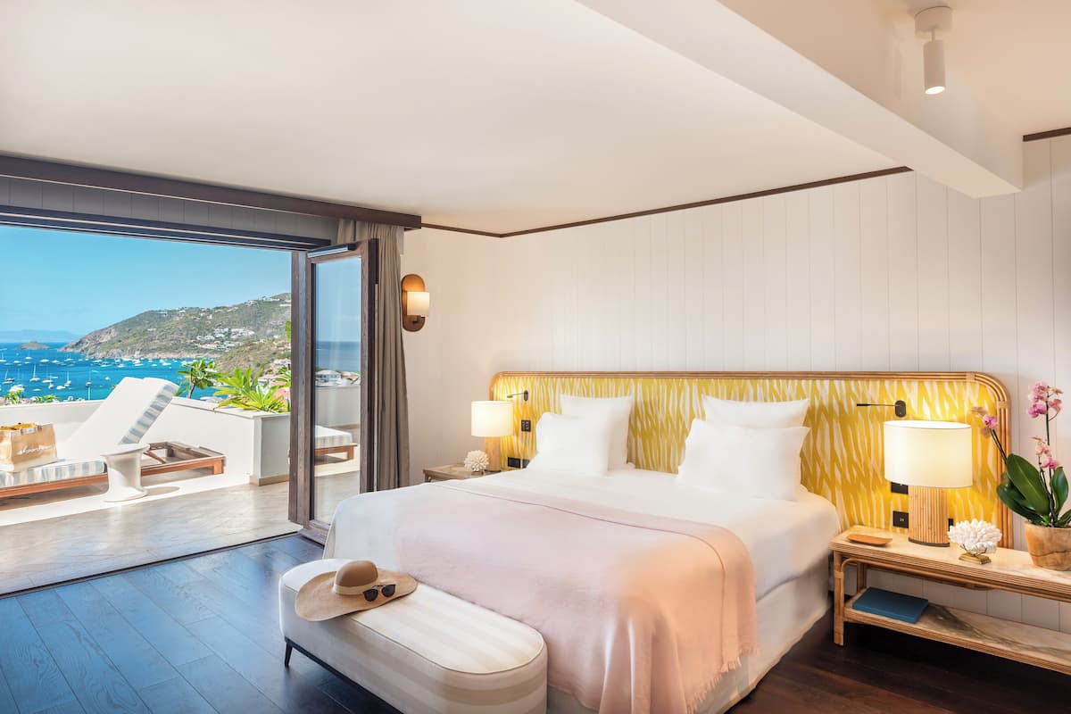 Ein modernes Hotelzimmer mit einem großen Bett, einem Nachttisch mit Lampe, Meerblick und einem Balkon mit Sitzgelegenheit.