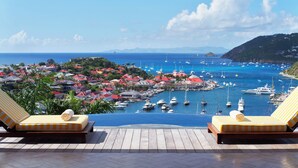 Une vue depuis un balcon donnant sur une marina, avec des bateaux, une ville côtière et un paysage montagneux en arrière-plan.