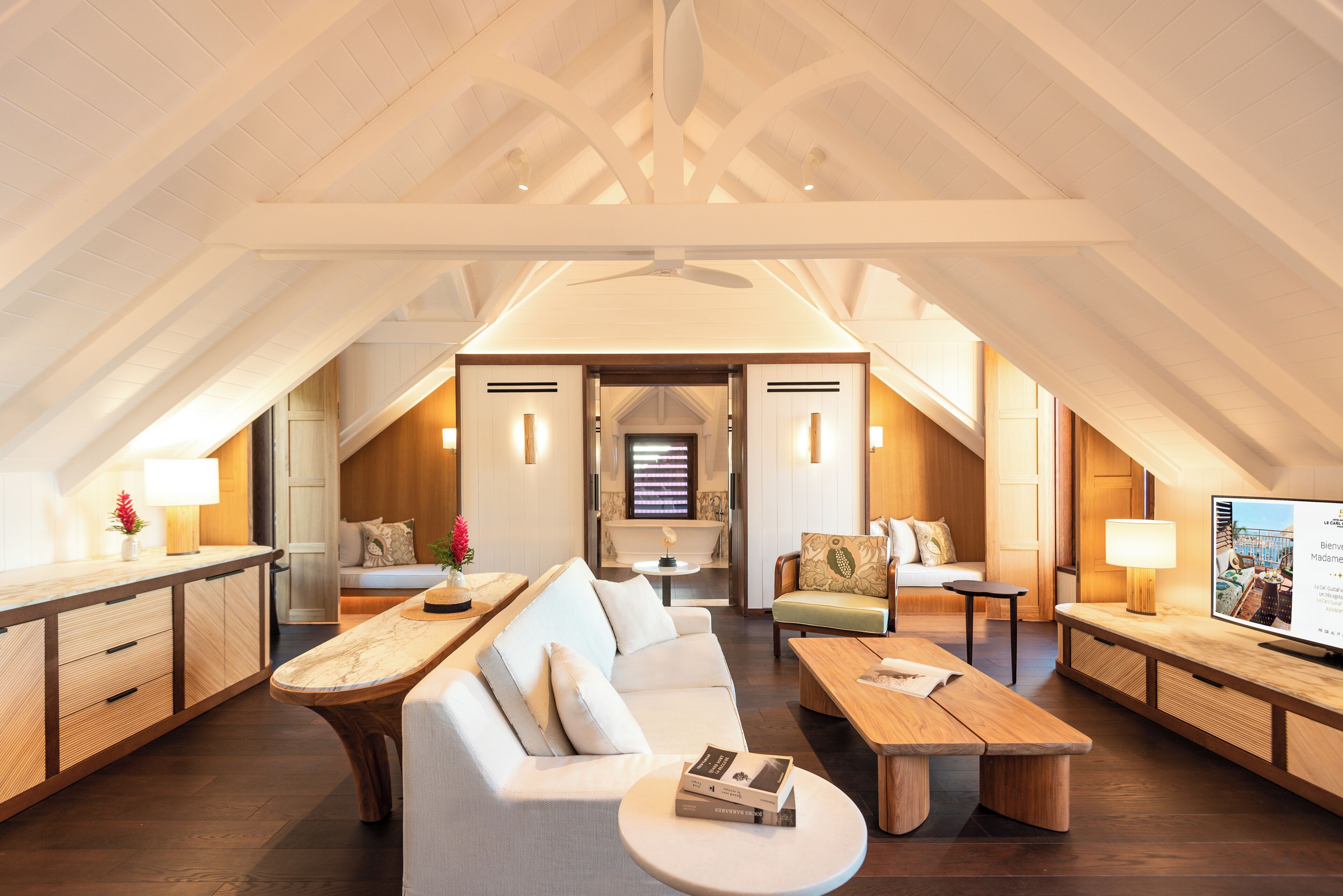 Un vaste espace de vie de style loft, doté d’un plafond haut, de poutres en bois, d’un grand canapé, d’une table à manger et d’un téléviseur.