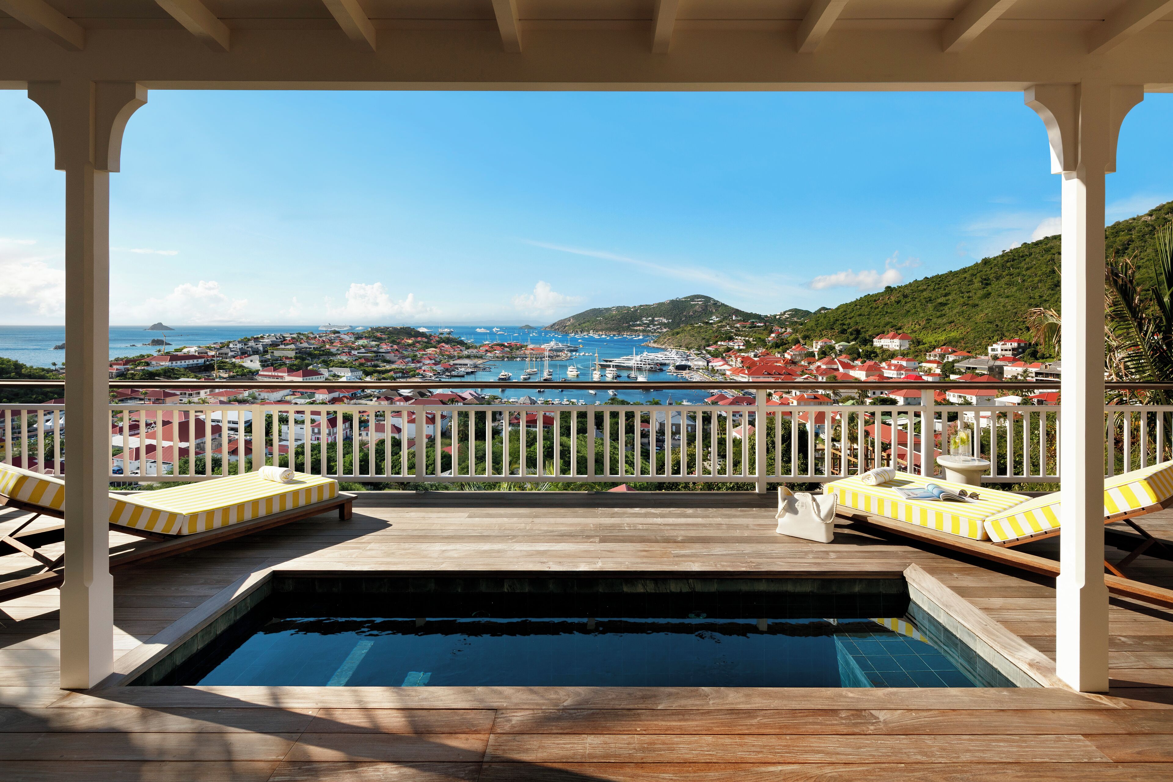A pool area with lounge chairs and a view of a coastal town.