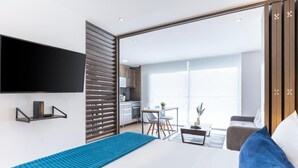Habitación de hotel moderna con una cama grande, un televisor montado en la pared, una kitchenette y un balcón con vistas.