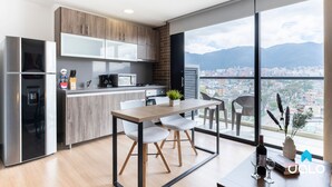 Una cocina moderna con comedor, ventanas amplias con vistas a la ciudad y un balcón con mesa y sillas.