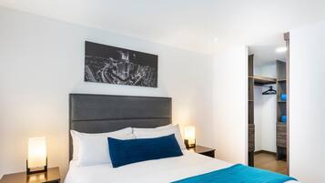 A modern hotel room with a large bed, a cityscape artwork on the wall, and a walk-in closet.