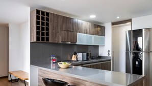 Una cocina moderna con alacenas de madera oscura, un refrigerador de acero inoxidable, un horno empotrado y una isla grande con un cuenco de fruta.