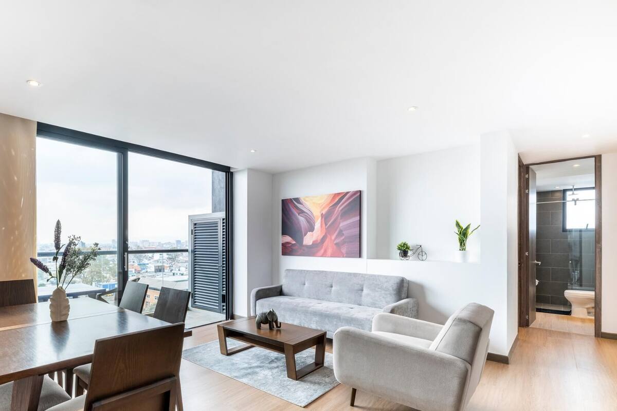 Sala moderna com área de jantar, janelas amplas, um sofá cinza e vista para a cidade.